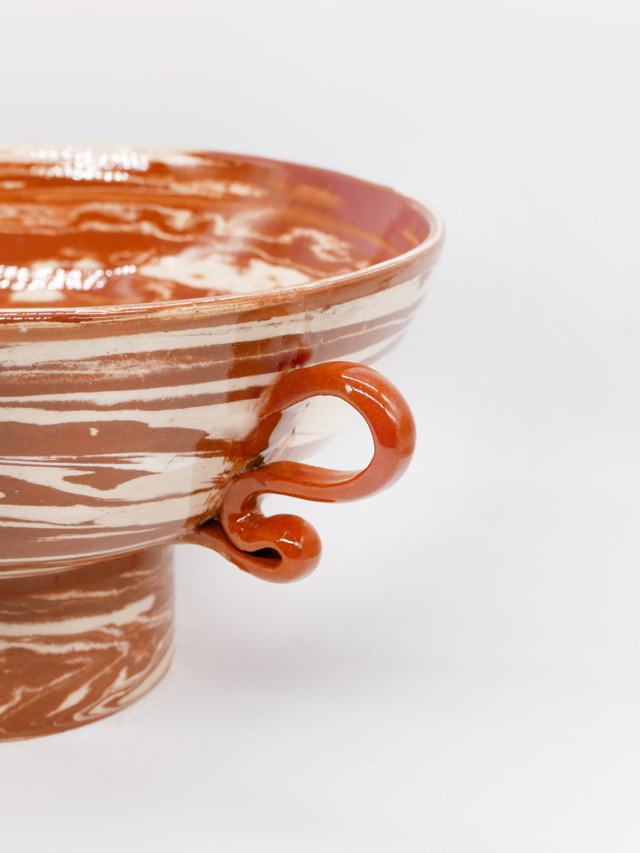 Ces objets en faïence émaillée sont entièrement façonnés à la main par un artisan-potier marocain travaillant dans l’Atlas. Gardien d’une tradition séculaire, il a repris l’atelier familial et perpétue un savoir-faire précieux. Les objets sont tournés un par un à la main en utilisant la technique des terres mêlées. Il s’agit de mélanger des argiles blanches et rouges afin de créer des motifs aléatoires marbrés ou zébrés dans des teintes naturelles terracotta. Chacun de ces objets est ainsi totalement unique