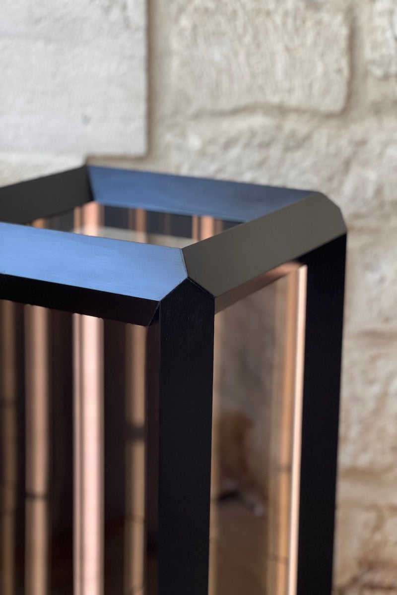 Fabriquée dans une structure en bois teinté noir Napoléon III, pour illustrer son interprétation conceptuelle de l'espace et de la lumière. Le verre sans tain de chaque facette dissimule un ensemble surprenant de miroirs et de lumières. Une fois activé, le rétro-éclairage laisse la magie opérer et le regard captivé pénètre dans un tunnel sans fin.