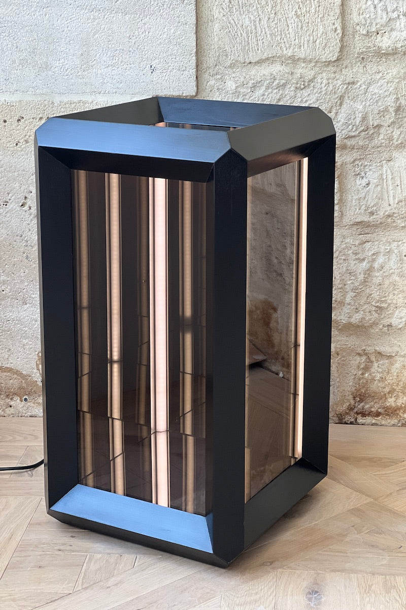 Fabriquée dans une structure en bois teinté noir Napoléon III, pour illustrer son interprétation conceptuelle de l'espace et de la lumière. Le verre sans tain de chaque facette dissimule un ensemble surprenant de miroirs et de lumières. Une fois activé, le rétro-éclairage laisse la magie opérer et le regard captivé pénètre dans un tunnel sans fin.