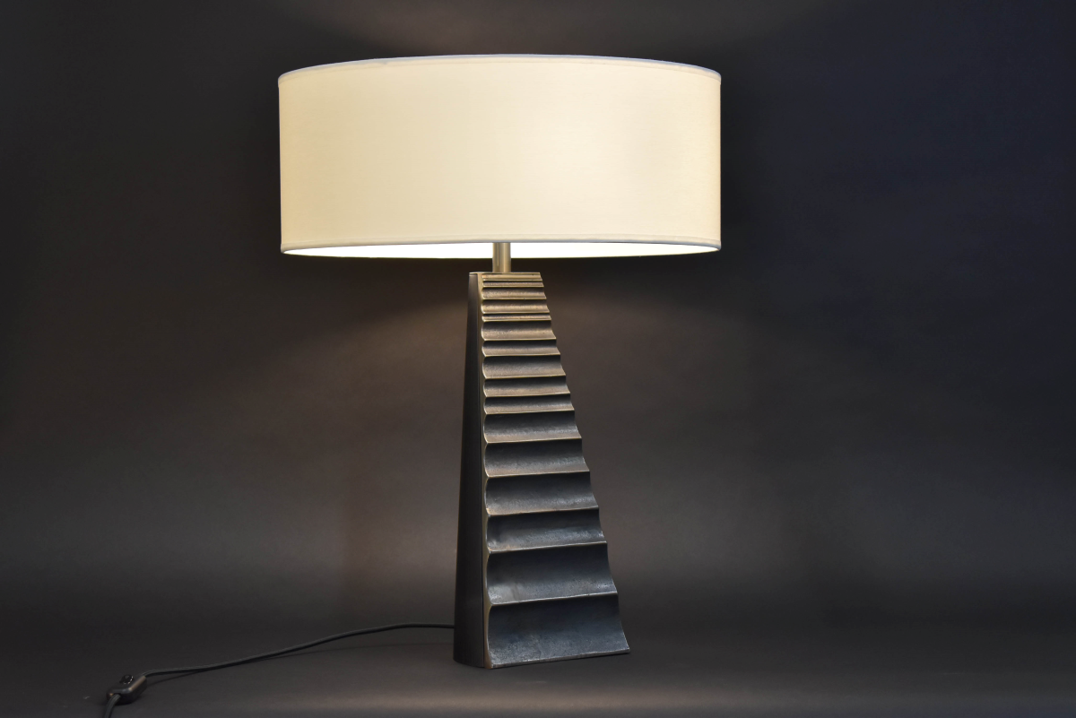 Cette lampe à poser Babel met en lumière une intention architecturalle et ammène à l'évocation d'un escalier immatériel. L'équilibre de cette lampe proposé par l'Atelier Demichelis tient à son contraste de matériaux et les subtils reflets de lumière dans le bronze parfois poli et parfoi mat. Cette pièce est proposée en édition limitée par Caroline Andréoni La Maison.