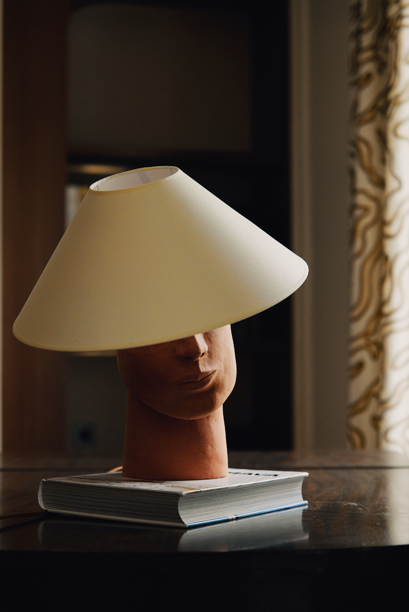 Fabriquée à base de grès orange brut chamotté, la lampe à poser Timide reprend un visage affirmé. Cette pièce fait partie du duo de lampes "Les Sœurs" proposé par l'artiste Thalia Dalecky.