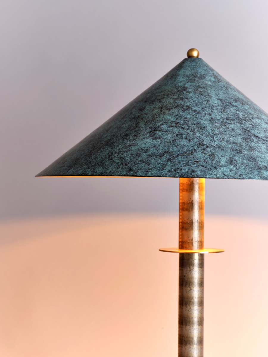 La lampe à poser Louisa incarne l'esthétique élégante et distinctive de Marine Breynaert, parfaite pour rehausser une table d'appoint dans un salon, un bureau ou une chambre. Fabriquée en laiton massif et aluminium thermolaqué, elle se distingue par son abat-jour en laiton patiné, offrant une teinte bleuâtre subtile et unique. Ce détail confère à la lumière une douceur singulière et crée une atmosphère apaisante.