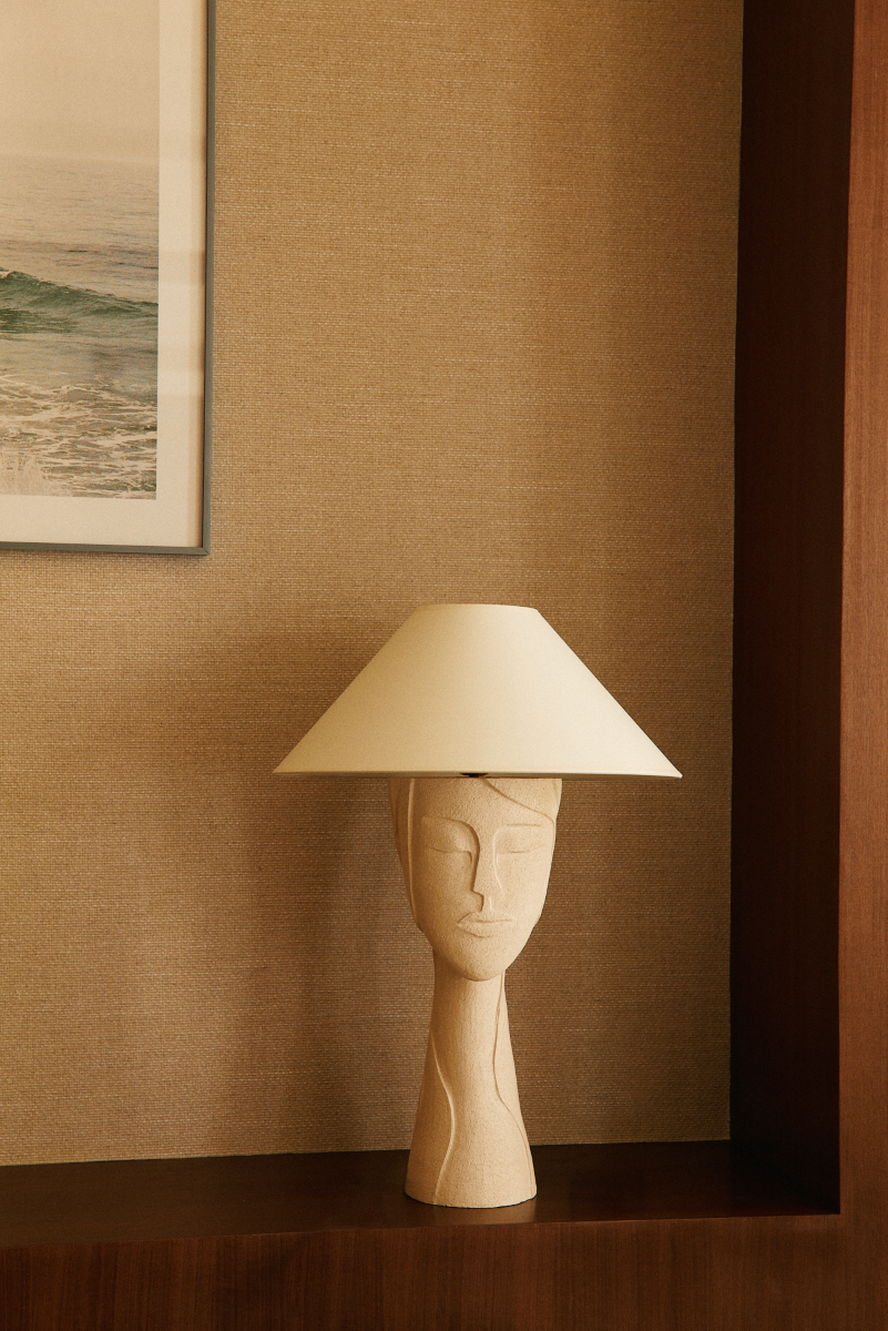 Représentant un visage gravé, la lampe Tranquille inspire à l'artiste Thalia Dalecky le calme d'un matin de printemps ensoleillé à son atelier, dans un silence apaisant.  Cette lampe à poser est confectionnée à base de grès blanc chamotté brut.
