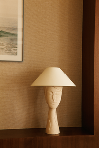 Représentant un visage gravé, la lampe Tranquille inspire à l'artiste Thalia Dalecky le calme d'un matin de printemps ensoleillé à son atelier, dans un silence apaisant.  Cette lampe à poser est confectionnée à base de grès blanc chamotté brut.