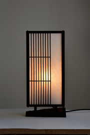 Véritable héritage de la culture japonaise traditionnelle, cette lampe puise son inspiration dans l’équilibre entre rigueur et douceur. Imaginée par le designer Thomas Coup La Fronde, elle associe la précision des savoir-faire artisanaux aux courbes organiques d’un pied en ébène massif. Les assemblages, subtilement révélés, témoignent d’une exigence rare tout en préservant une esthétique épurée et intemporelle.