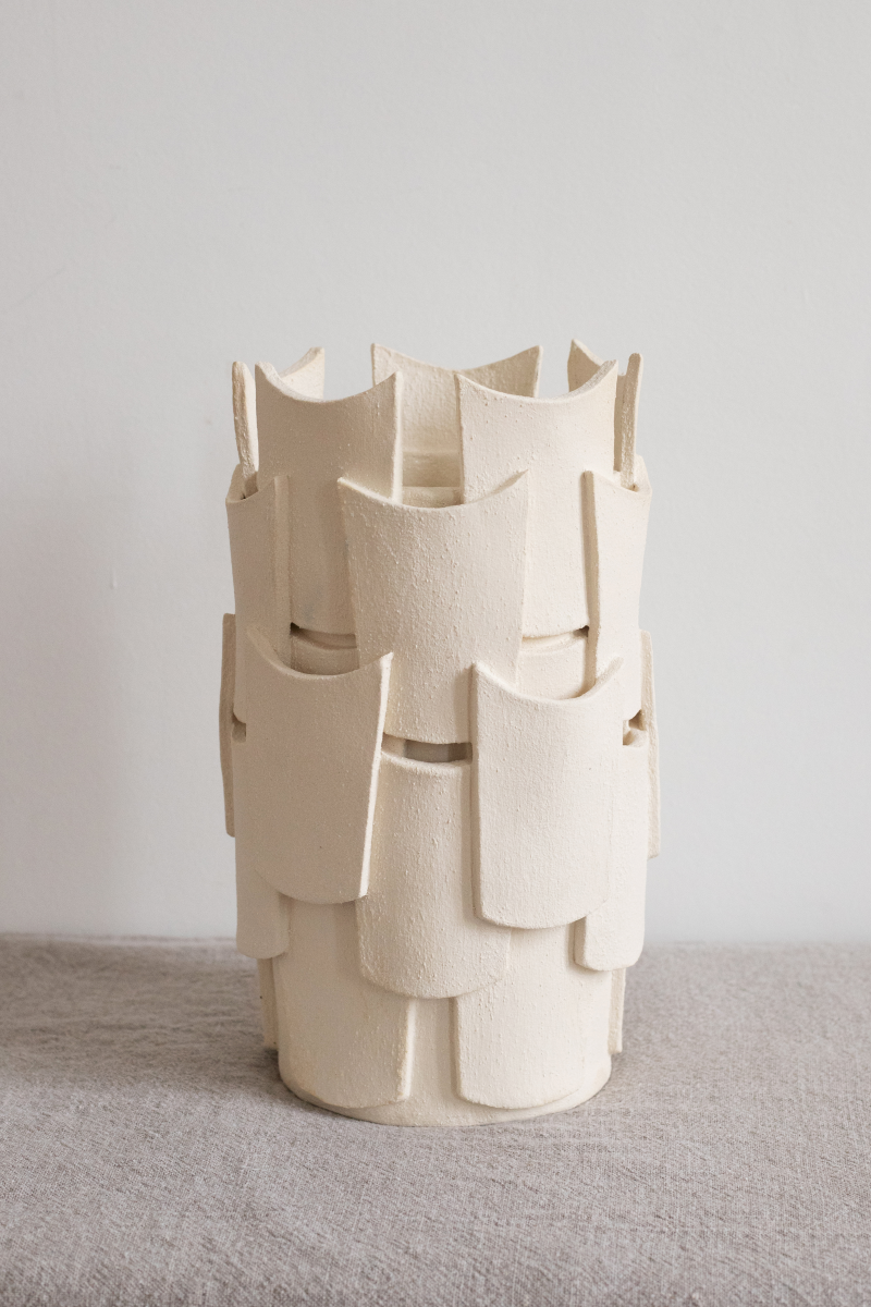 Le vase en petit modèle est fabriqué avec du grès blanc chamotté, terre lisse à laquelle a été rajoutée de la terre cuite broyée, lui donnant une texture idéale pour le modelage et un grain authentique. Cette pièce réalisée selon la technique de la plaque est le résultat du savoir-faire de la créatrice, entièrement confectionnée à la main dans ses ateliers en France.