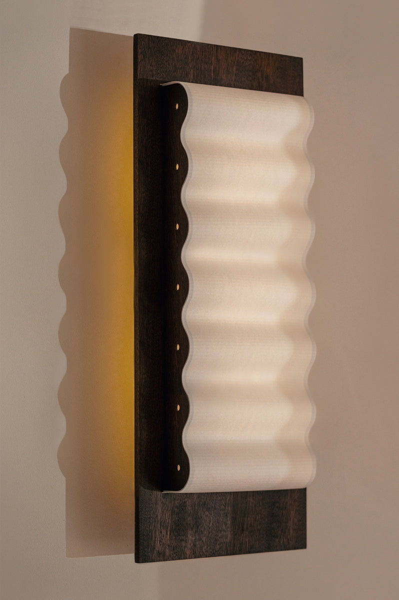 Les appliques Frame Wood de Violaine d'Harcourt sont fabriquées à la main au Portugal avec du bois d'acajou huilé et du papier.

Dotées d'un design minimaliste et rendant un subtil hommage à l'architecture moderne, les appliques murales Frame sont réalisées avec des matériaux contrastés qui rehaussent le toucher doux d'une vague de papier.