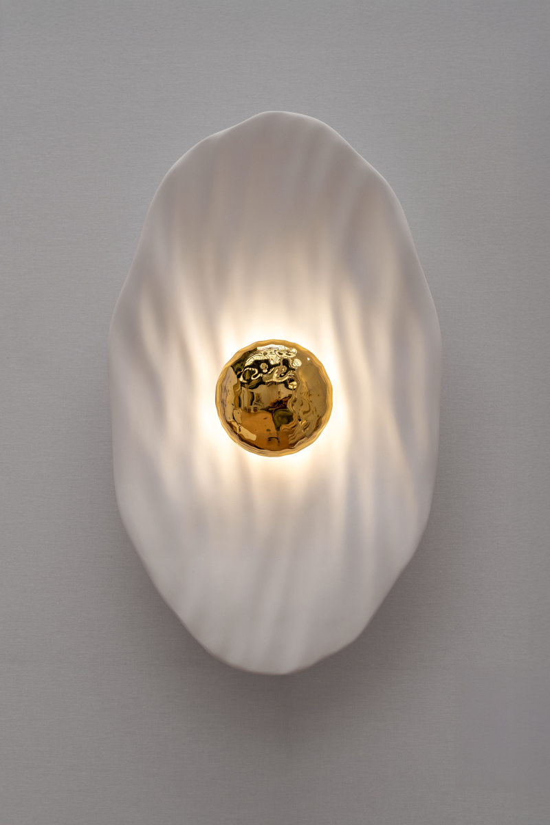 Façonnée à la main, l’applique Vesta associe un disque en faïence émaillée doré 24K, à une structure en plâtre sculpté aux lignes organiques.

Conçue comme une offrande à la lumière, Vesta rend hommage à la déesse du foyer. Elle diffuse une lumière douce et enveloppante, idéale pour instaurer une atmosphère apaisante et sacrée.