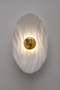 Façonnée à la main, l’applique Vesta associe un disque en faïence émaillée doré 24K, à une structure en plâtre sculpté aux lignes organiques.

Conçue comme une offrande à la lumière, Vesta rend hommage à la déesse du foyer. Elle diffuse une lumière douce et enveloppante, idéale pour instaurer une atmosphère apaisante et sacrée.