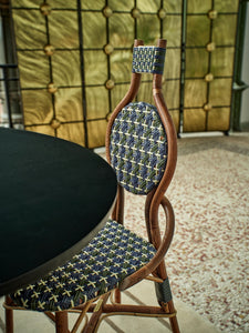 La chaise Odette fait la part belle au rotin. Le Second Empire a vu se développer le métier de rotinier et a été l’âge d’or de ce matériau. Le rotin est une tige de palmier importée des forêts tropicales asiatiques à l’époque coloniale. La chaise de bistro en rotin symbolise à elle seule les terrasses parisiennes et la gaieté de la capitale française. La forme florale et l’utilisation de matières végétales pour le design de la chaise Odette est une référence au catleya.