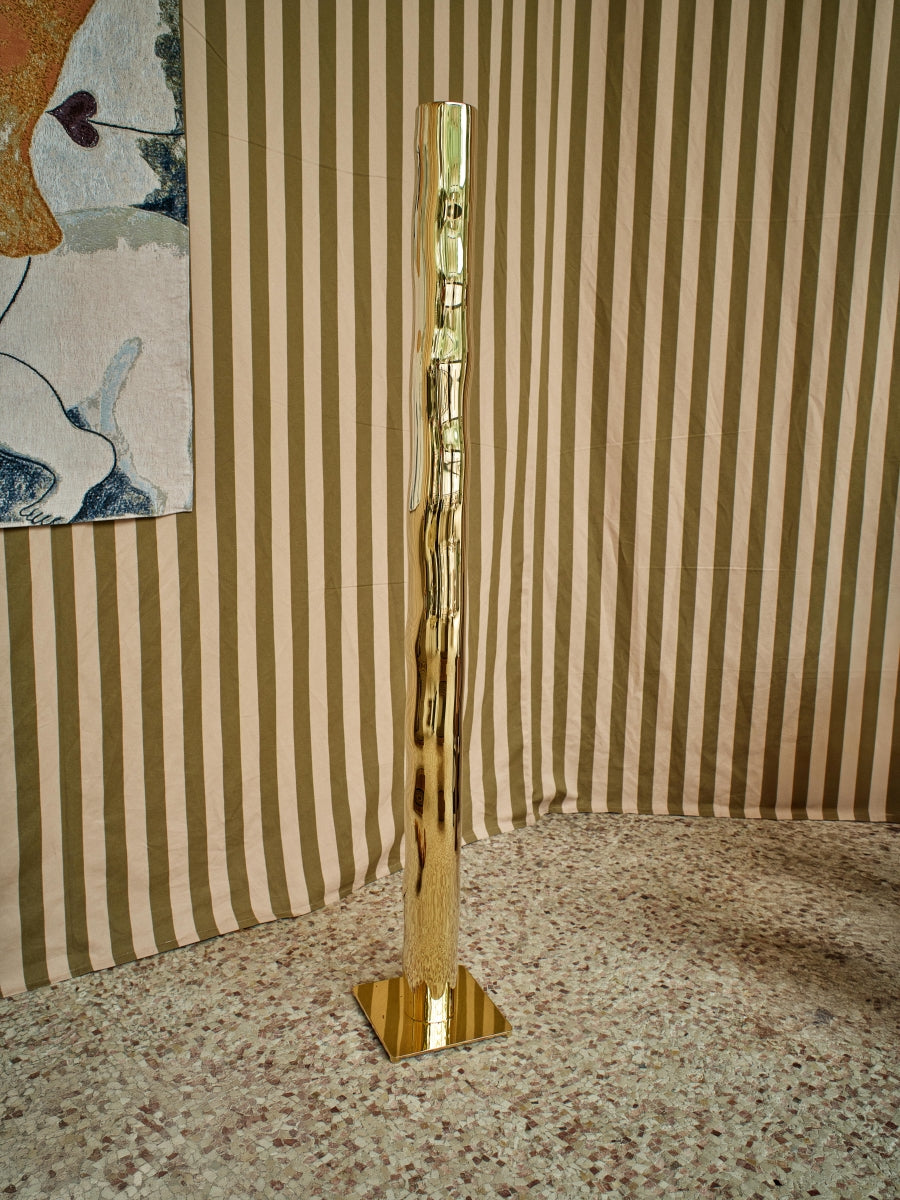 Hélios est un lampadaire sculptural en laiton poli miroir, non verni. Sa source lumineuse, dissimulée, diffuse une lumière douce vers le haut. Entièrement formée, soudée et polie à la main, chaque pièces de cette série sont uniques. Le reflet de sa hauteur dans son socle crée une illusion de mouvement, d’infini, un jeu de perceptions où le vertige s’invite. Hélios transforme l’espace, oscillant entre objet fonctionnel et œuvre sculpturale.