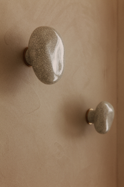 La patère Agate tire son nom de la pierre précieuse éponyme. Chaque patère possède sa propre personnalité, accentuée par les émaux cristallisés ou colorés qui s’harmonisent avec sa forme douce et organique, reflétant la diversité des teintes présentes dans les pierres d’Agate.  Son design intemporel et organique évoque la beauté et la simplicité des galets, tandis que sa délicate base est ornée d’une bague en laiton brossé.