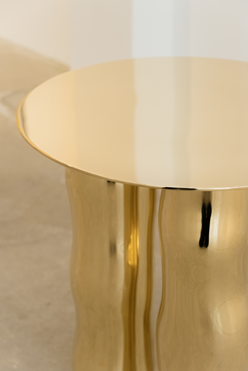 Mimo est une table d’appoint en laiton poli miroir, non verni. Sa structure repose sur une intention formelle simple : trois pieds et un plateau. Ses pieds, formés de manière organique, contrastent avec la ligne fine et délicate de son plateau.

La surface polie capte la lumière et reflète l’environnement, révélant l’élégance contenue dans la simplicité. Le laiton, travaillé à la main, invite à une expérience sensorielle où la matière et l’espace entrent en conversation.