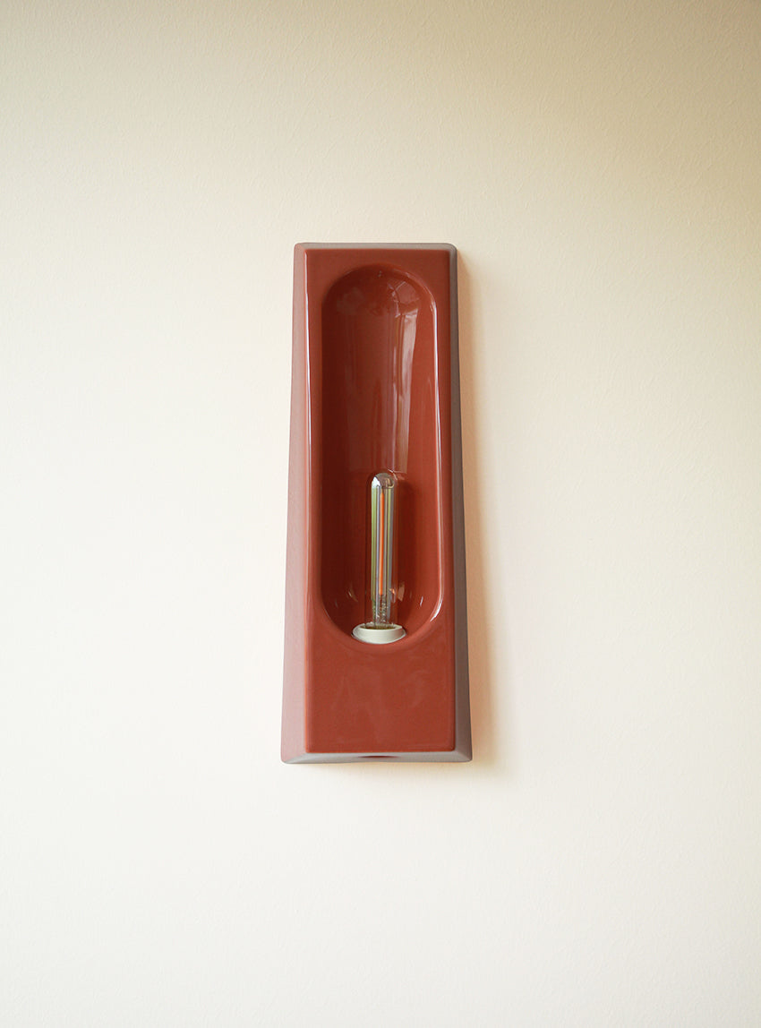 Alliance de l'artisanat et du design contemporain, les appliques Alcove de Violaine d'Harcourt sont fabriquées en céramique émaillée au Portugal, dans une région où le travail de l'argile est une tradition ancestrale. Leur forme s'inspire de l'élément architectural auquel elles ont emprunté leur nom - l'alcôve - qui évoque une ambiance intimiste et feutrée. Au centre de l'applique, une élégante ampoule tubulaire diffuse une lumière tamisée qui sublime les émaux aux teintes naturelles.&nbsp;