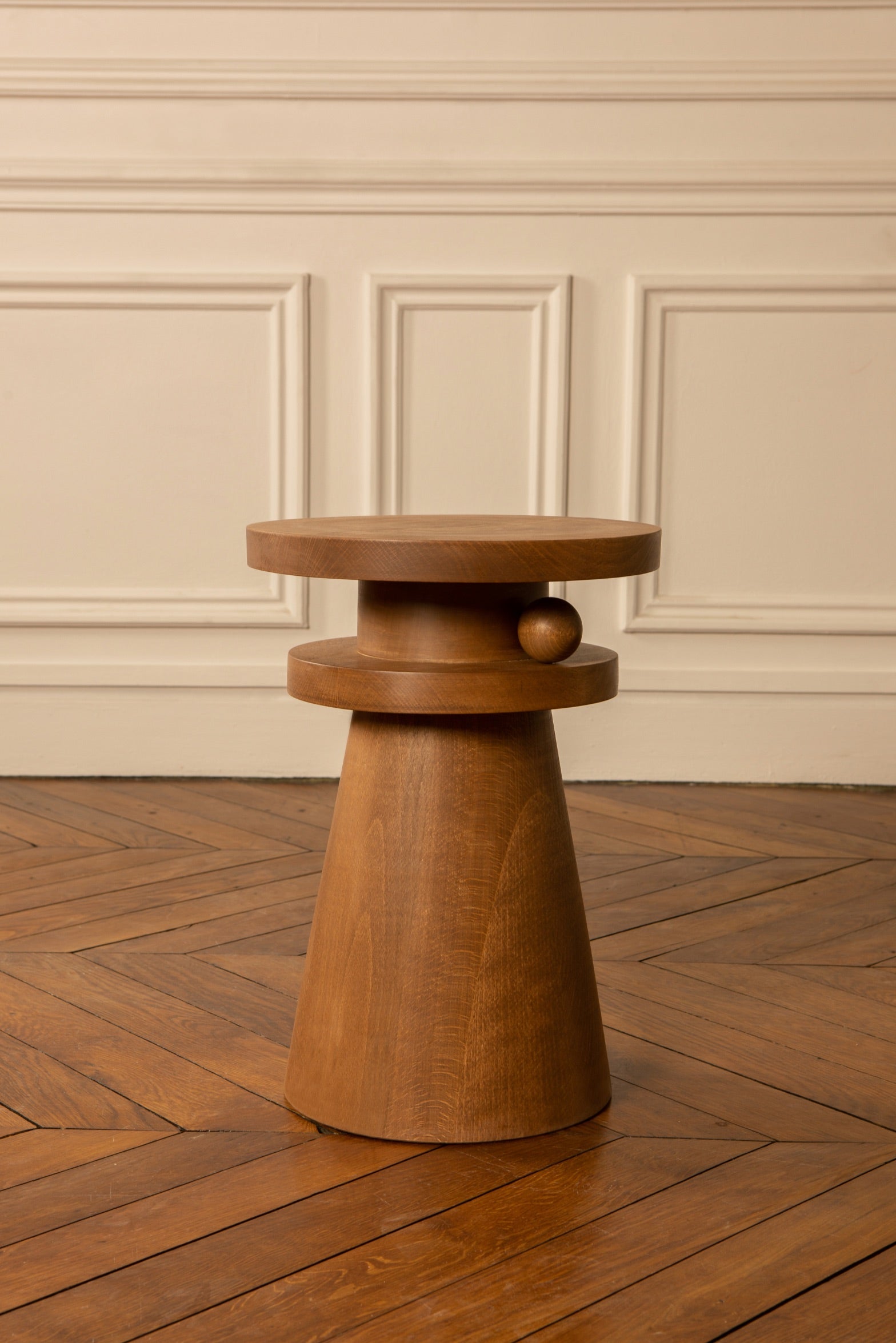 Joya est un objet de décoration nomade aux multiples usages. Tabouret, table d'appoint, bout de canapé, table de chevet, il a été conçu pour vous au quotidien selon vos envies et vos besoins suivre.   Il est décoré d'une boule sculptée entre ses deux plateaux, détail géométrique en asymétrie. Elle semble être posée délicatement, presque en mouvement : le gage d'un travail soigneux et minutieux.